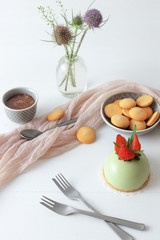Table with no-bake strawberry mini sphere matcha cheesecake embellished with real fresh strawberry and leaves of rosemary with bowl of salt caramel, buiscuits and glass vase with wild teasel flowers.
