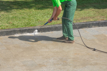 Worker man in uniform washes street or park sidewalk. Municipal service of city cleaning process....