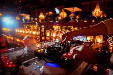 music controller DJ in the booth on the background of the dance floor with dancing people at the...