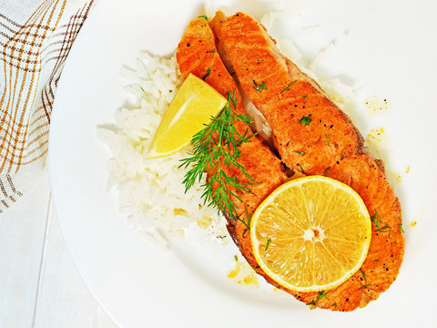 Pan seared salmon fillet steak with rice, lemon, garlic and dill on white plate, flat lay, top view.