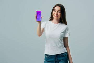 happy beautiful girl in white t-shirt showing smartphone with online shopping app isolated on grey