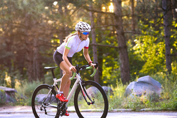 Young Woman Cyclist Riding Road Bicycle on the Free Road in the Forest at Hot Summer Day. Healthy Lifestyle Concept.