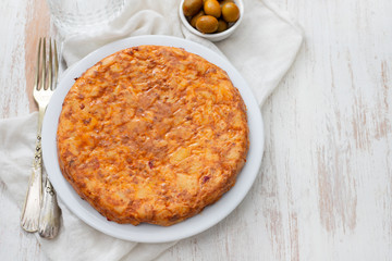 Traditional spanish food Tortilla with potato on white dish and olives in small bowl on ceramic background.