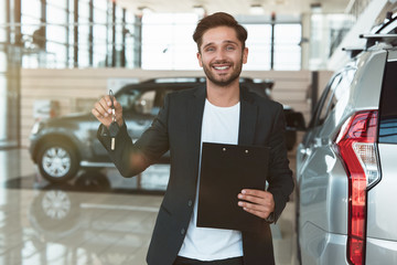 young handsome man manager smiling with brochure in his hand standing in dealership center near...