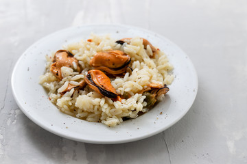 rice with mussels on small white plate on ceramic background