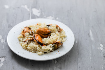 rice with mussels on small white plate on ceramic background