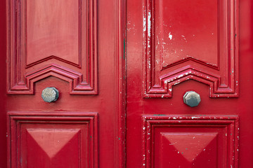 Red wooden door. Bright red painted wooden door with geometric frames and peeling paint. Symmetric double door decorations and two old metal doorknobs. Architectural background. Vintage textures