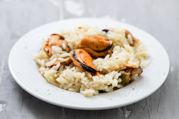 rice with mussels on small white plate on ceramic background