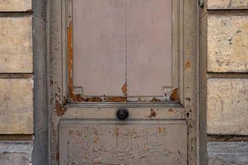 Old wooden door. Details of old shabby wooden door with flaking paint of grey color. Black circle doorknob in center of dusty door on stone walls. Grunge textures of aged painted wood surface closeup 