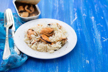 rice with mussels on small white plate on blue wooden background