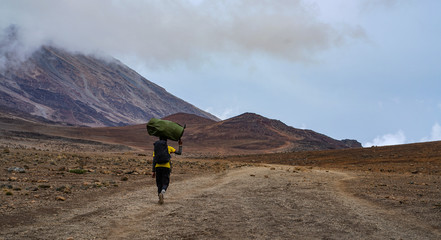 Porter Carrying Heavy Stuff On His Head, Trekking Kilimanjaro Mountain, Kilimanjaro National Park, Tanzania © natanaelginting