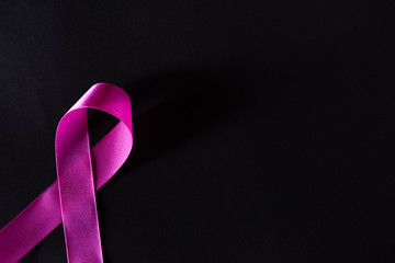 Pink ribbon on black paper background for supporting breast cancer awareness month campaign.