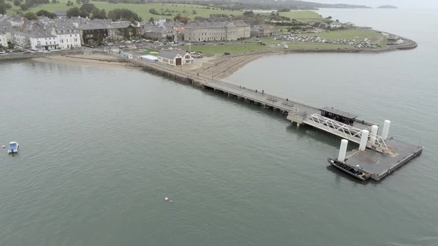 Beaumaris Seaside town With Pier And Coast, Wales. Aerial view low pull back reveal across Menai Strait tourist coastline.