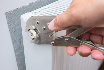 Plumber with wrench repairs a metal heating radiator forming part of a central heating system with...