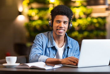 Cheerful teen guy with headset working with laptop