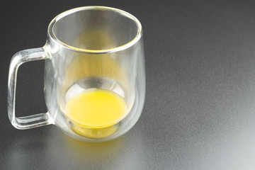 Close up transparent clear glass mason cup with little orange juice on dark background and copy space.