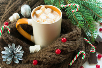 Cup of hot cocoa or chocolate with marshmallows on the background of a knitted scarf and Christmas tree branches. Traditional drink for the Christmas holidays. Close-up. New Year background.
