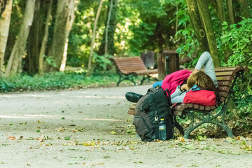 young man resting on bench with backpack on the floor