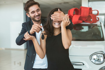 young handsome man makes surprise for his beautiful wife closes her eyes with his hands standing in...