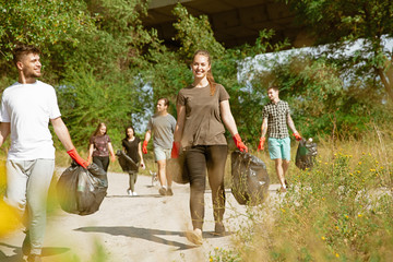 Team of building the future. Group of volunteers tidying up rubbish on beach in sunny day. Young men and women take care of nature and environment, taking bottles and packs away. Concept of ecology.