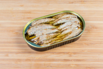 Canned sprats in open tin can on wooden surface