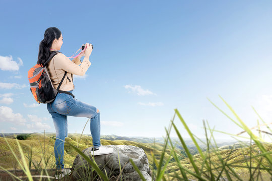 Rear view of Asian woman with a backpack holding a camera to take pictures