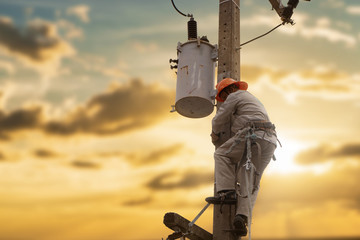 Silhouette electrician working maintenance equipment on  electric pole in sunset background.