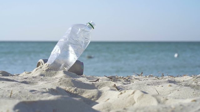 Plastic bottle in the sand near the sea. Slowmotion. Ecology concept.
