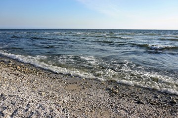 Wavy seascape view from the beach with pebbles and seashells on it.
