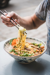 Man having dinner at vietnamese restaurant. Man eating fresh cooked vietnamese noodle curry with duck with bamboo chopsticks from beautiful Asian porcelain plate. Asian, oriental fastfood cuisine