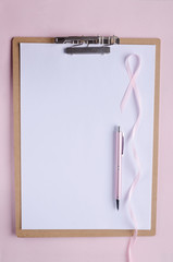 Fototapeta na wymiar Clipboard, white blank paper, pink pen and pink ribbon as a symbol of breast cancer.Pink background, empty space for text