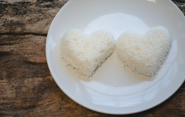 Jasmine rice is arranged in two heart shapes in white dish and on a old wooden table and black background, Selective focus, Vintage style.