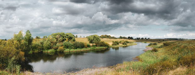 Beautiful panoramic landscape with river and dark stormy clouds over the land