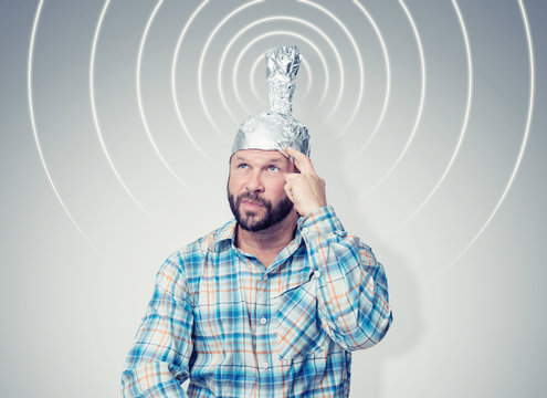 Bearded funny man in a cap of aluminum foil sends signals. Concept art phobias