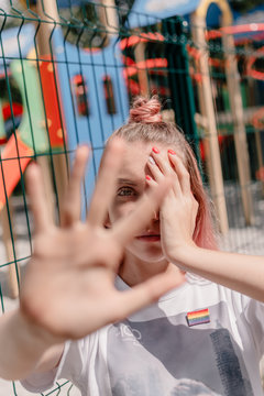 Outdoor portrait of young teenager hipster girl with pink hair and lgbt sign. young woman with LGBT rainbow sign shows stop sign with hands. LGBTQ youth, lgbt gay pride tolerance concept