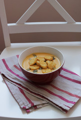 homemade mashed pumpkin soup with crackers in a red bowl on a white towel in red and green stripes on a white chair in bright colors 