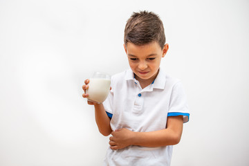 Little boy with dairy allergy holding glass of milk indoors. Child with painful expression after...