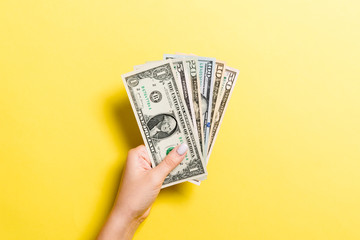 Top view of female hand giving various dollar bills on colorful background. Charity and donation concept