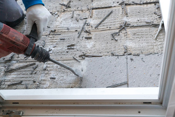 construction worker using a handheld demolition hammer and wall breaker to chip away and remove old...