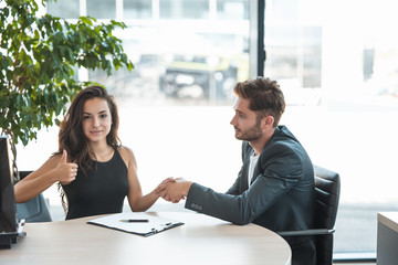 beautiful young woman manager shows like sign shaking hands with handsome man client after holding succesful business purchase deal at the office