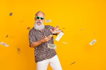 Portrait of crazy funny funky old long bearded man millionaire in eyewear eyeglasses waste money throw banknotes wear leopard shirt shorts isolated over yellow background - obrazy, fototapety, plakaty