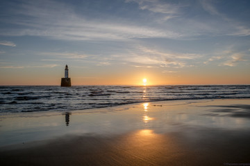 Sunrise on a beach with a lighthouse inside the sea