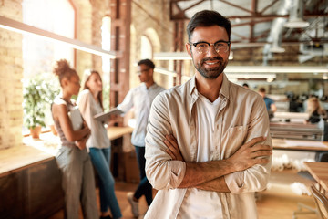 Great working day! Young bearded man in casual clothes keeping arms crossed and looking at camera...