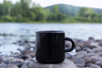 Black campfire mug mockup with stony river bank