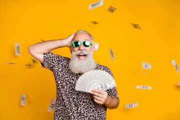 Portrait of retired old funny bearded man in eyewear eyeglasses scream omg look at falling money win lottery wearing leopard t-shirt isolated over yellow background