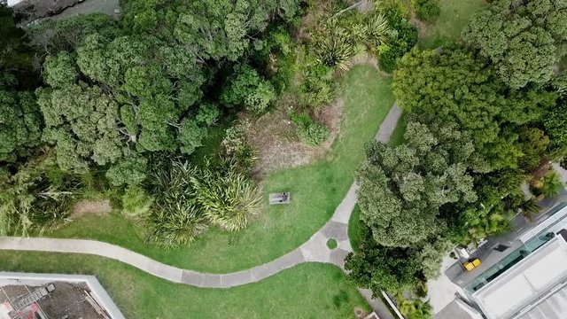 Aerial birds eye view above ocean beachfront grass recreational park land, rising drone view above pathways & over house rooftops.