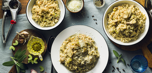 banner of Classic Italian risotto with mushrooms on a wooden table with a blue linen tablecloth. red wine. bottle and glasses. top shots