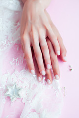 woman hands with manicure among white lace on pink background, cosmetic concept