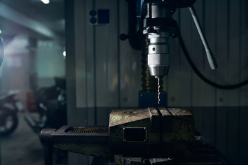 Drill in the chuck of a drilling machine in a motorcycle workshop. Close-up.