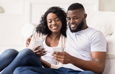 Fototapeta premium Smiling couple scrolling photos in smartphone together sitting at home